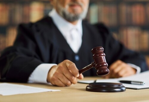 judge in robes striking wooden gavel on sound block at courtroom desk