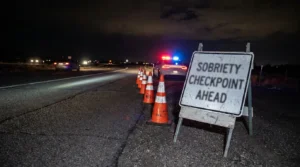 Sobriety Checkpoint Ahead sign with traffic cones and police vehicle at night